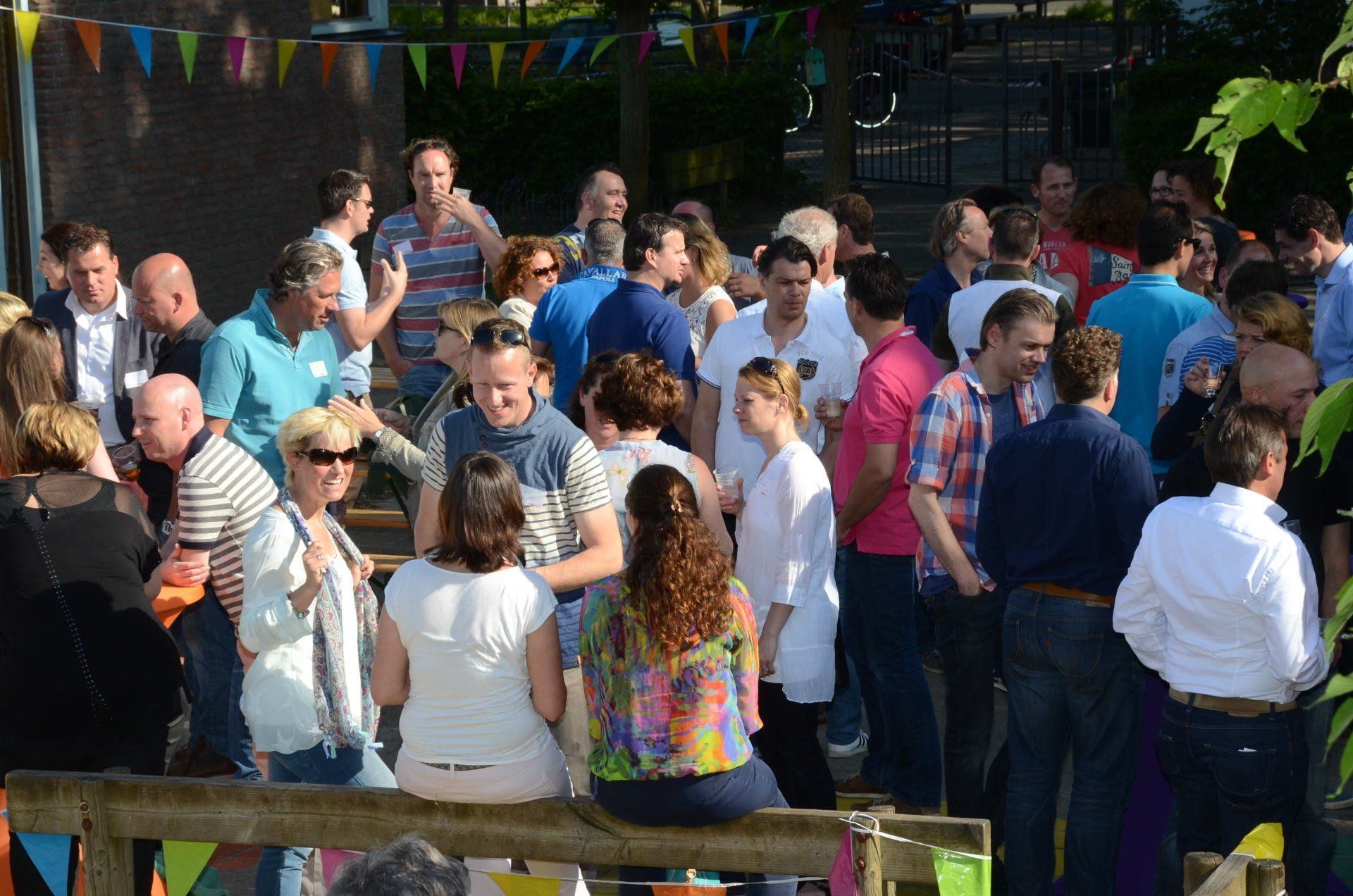 Een groep mensen, mogelijk bij een evenement, stond buiten bij een hek. De meesten droegen vrijetijdskleding.