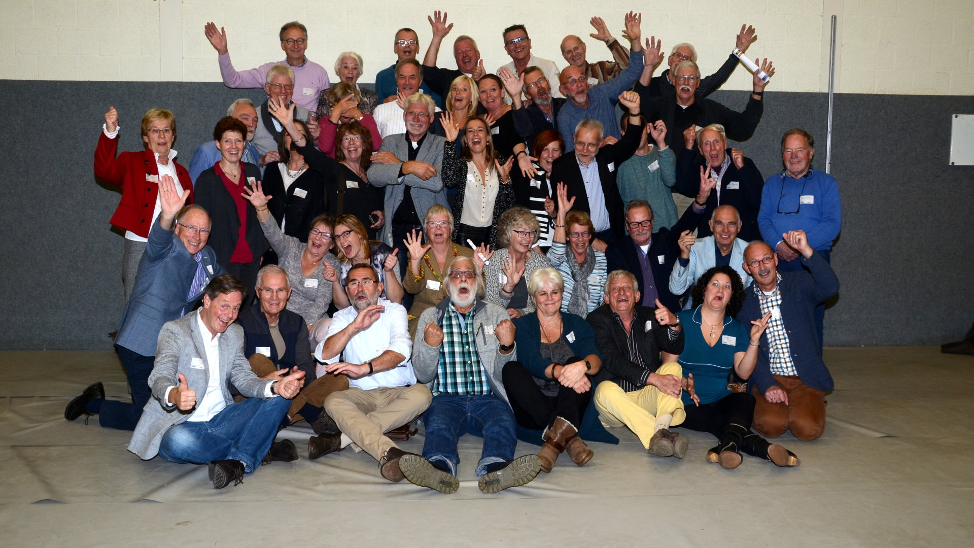 Een groep mensen lacht en zwaait binnen.