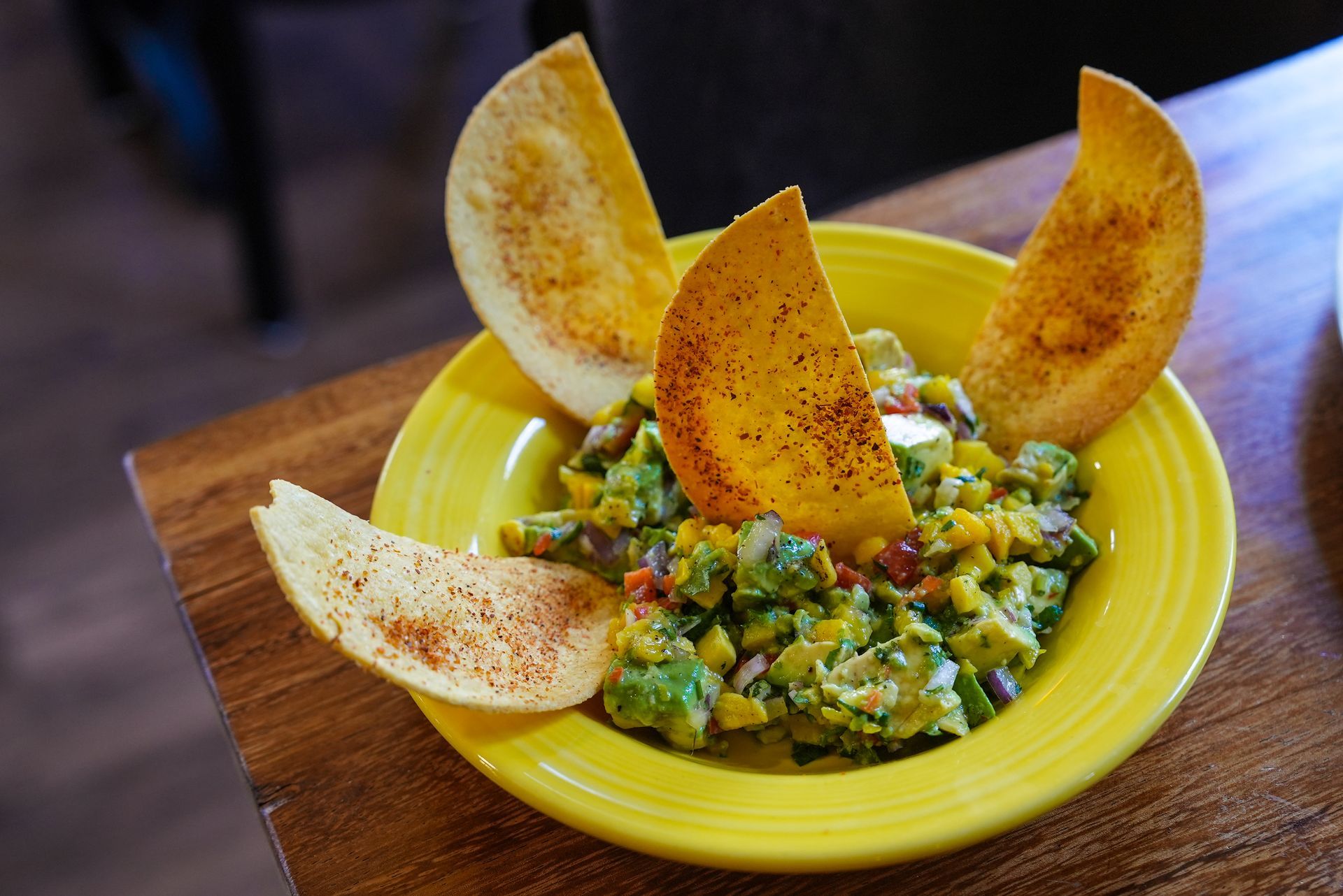 A yellow bowl of guacamole with tortilla chips on top