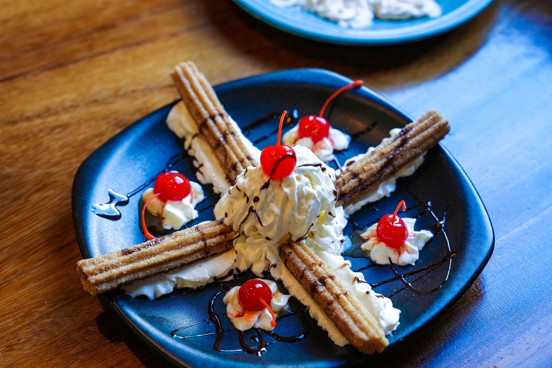 A plate of churros with whipped cream and cherries on top