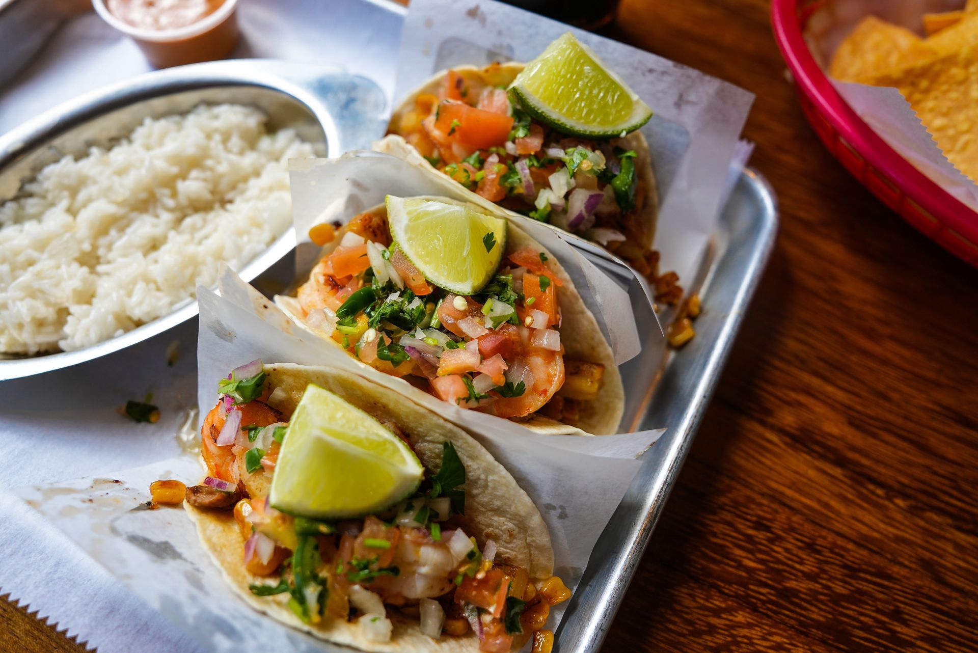A tray of tacos with limes and rice on a table