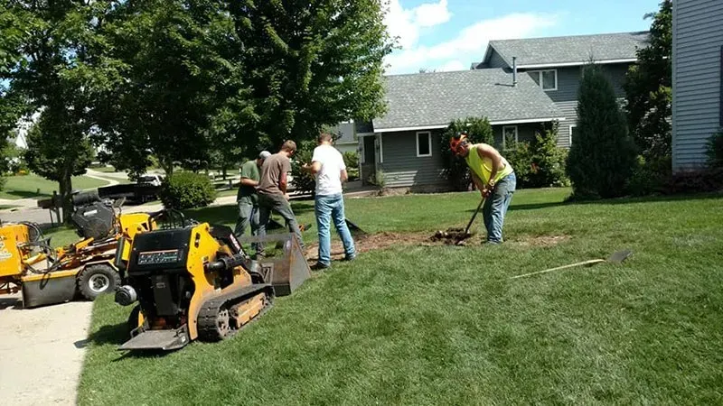Four workers use a trencher and shovels to dig a trench in a suburban front yard.