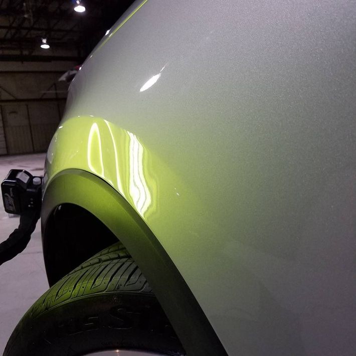 Close-up of a white car’s front wheel and fender with a yellow reflection.