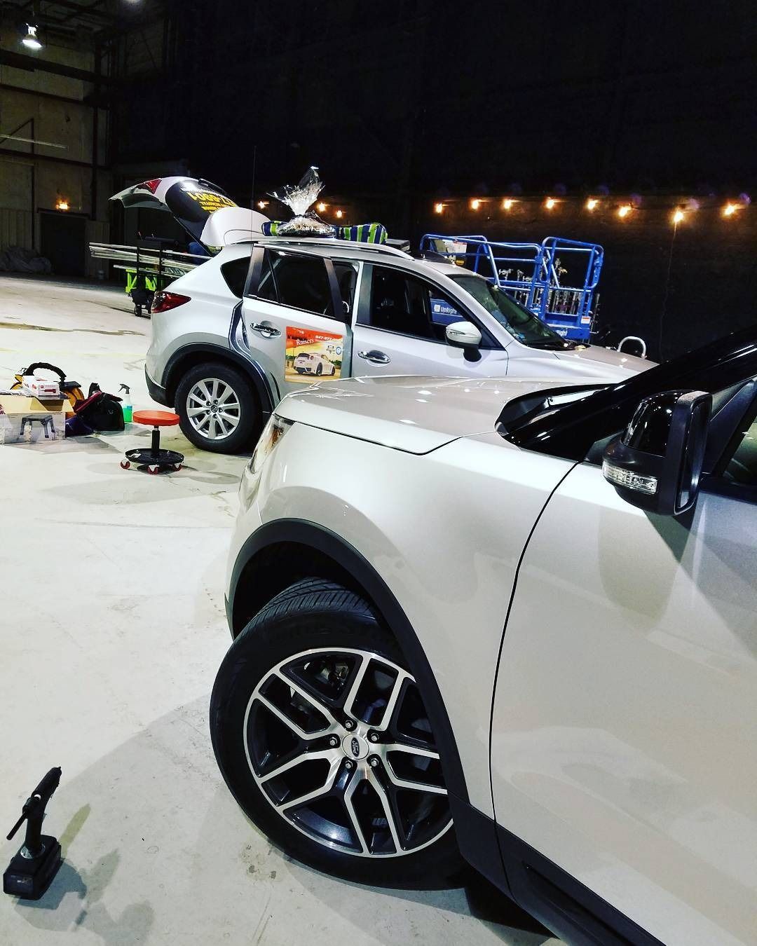 White SUV and other vehicles in a lit indoor garage, with tools on the floor