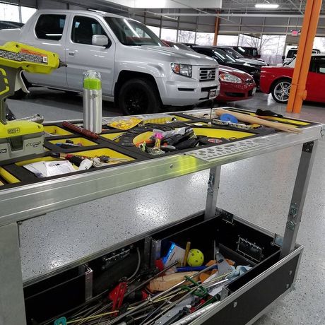 Workbench with tools and open drawer in a parking garage, with a white pickup truck and other cars in the background