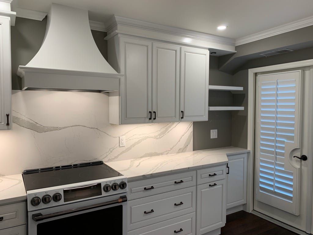 A kitchen with white cabinets , a stove , and a door.