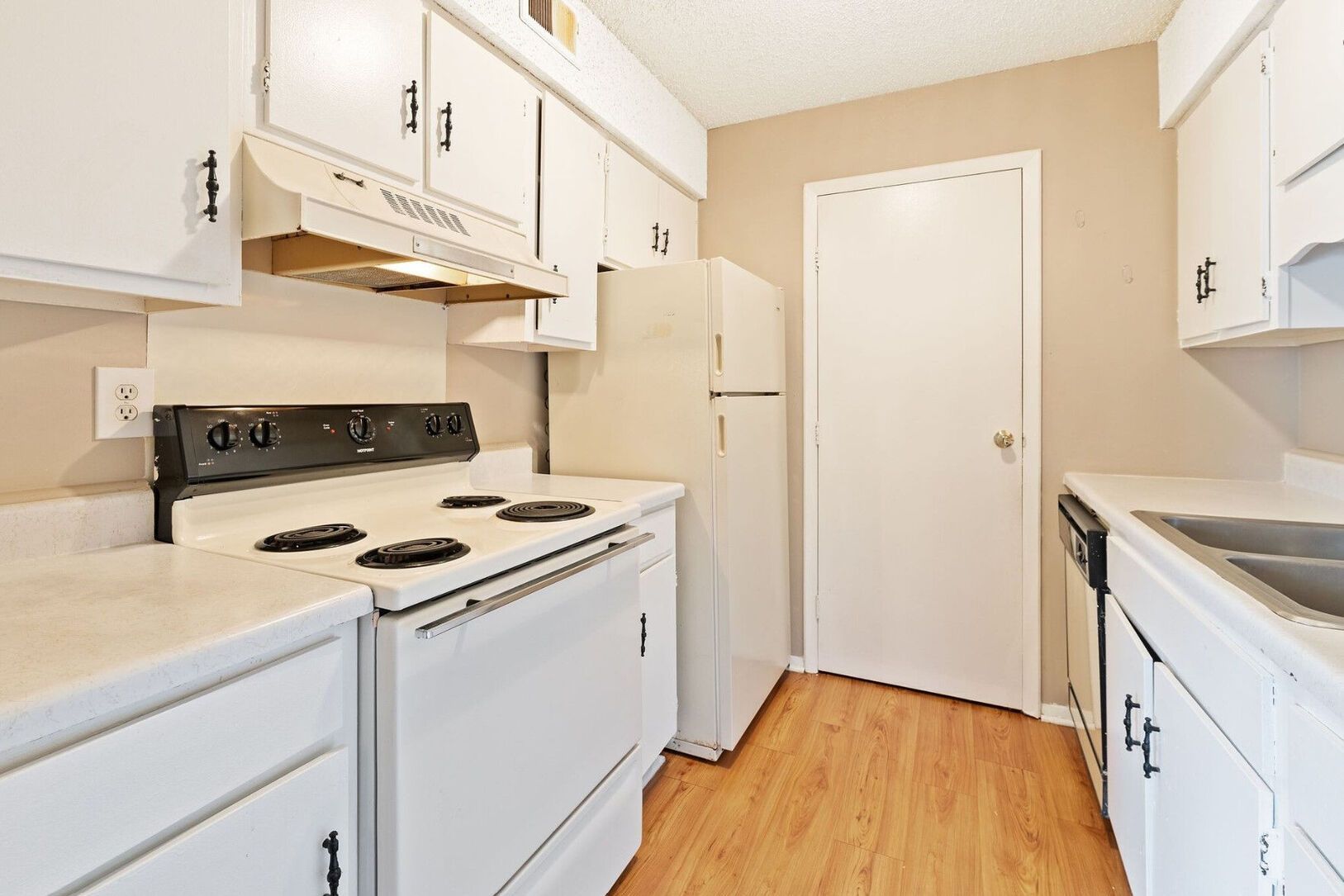 White kitchen with cabinets, stove, refrigerator, and sink, with a white door.