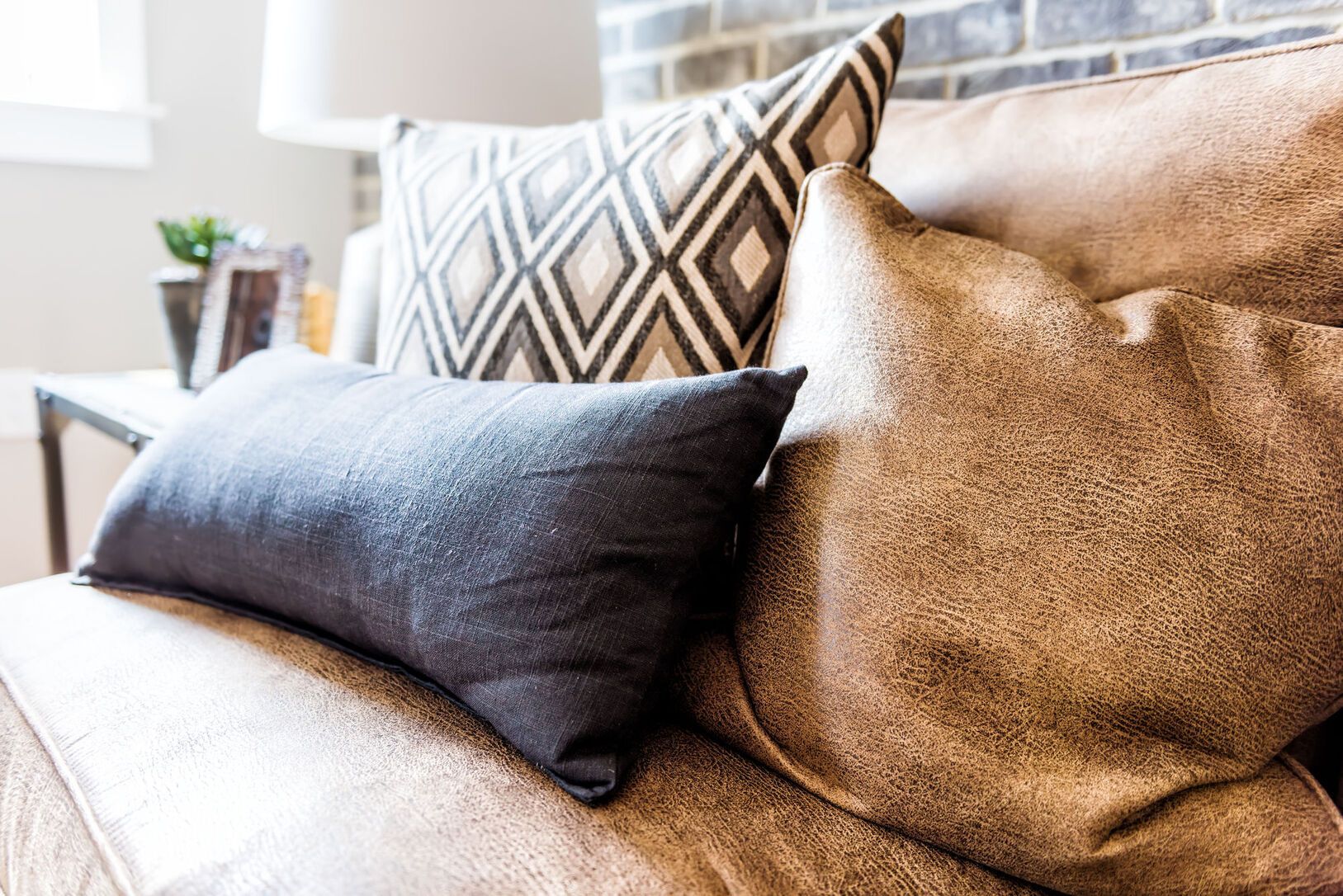 Couch with several pillows in shades of brown, black, and a diamond pattern. A side table is in the background.