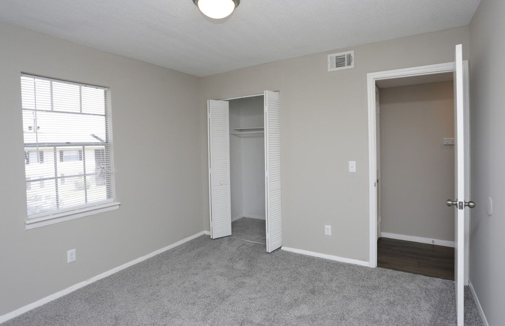 A light-filled bedroom with gray walls, a closed window, closet, and open door to another room.