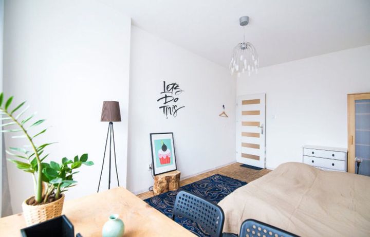 Bright bedroom with a bed, a potted plant, a floor lamp, and artwork on the wall.