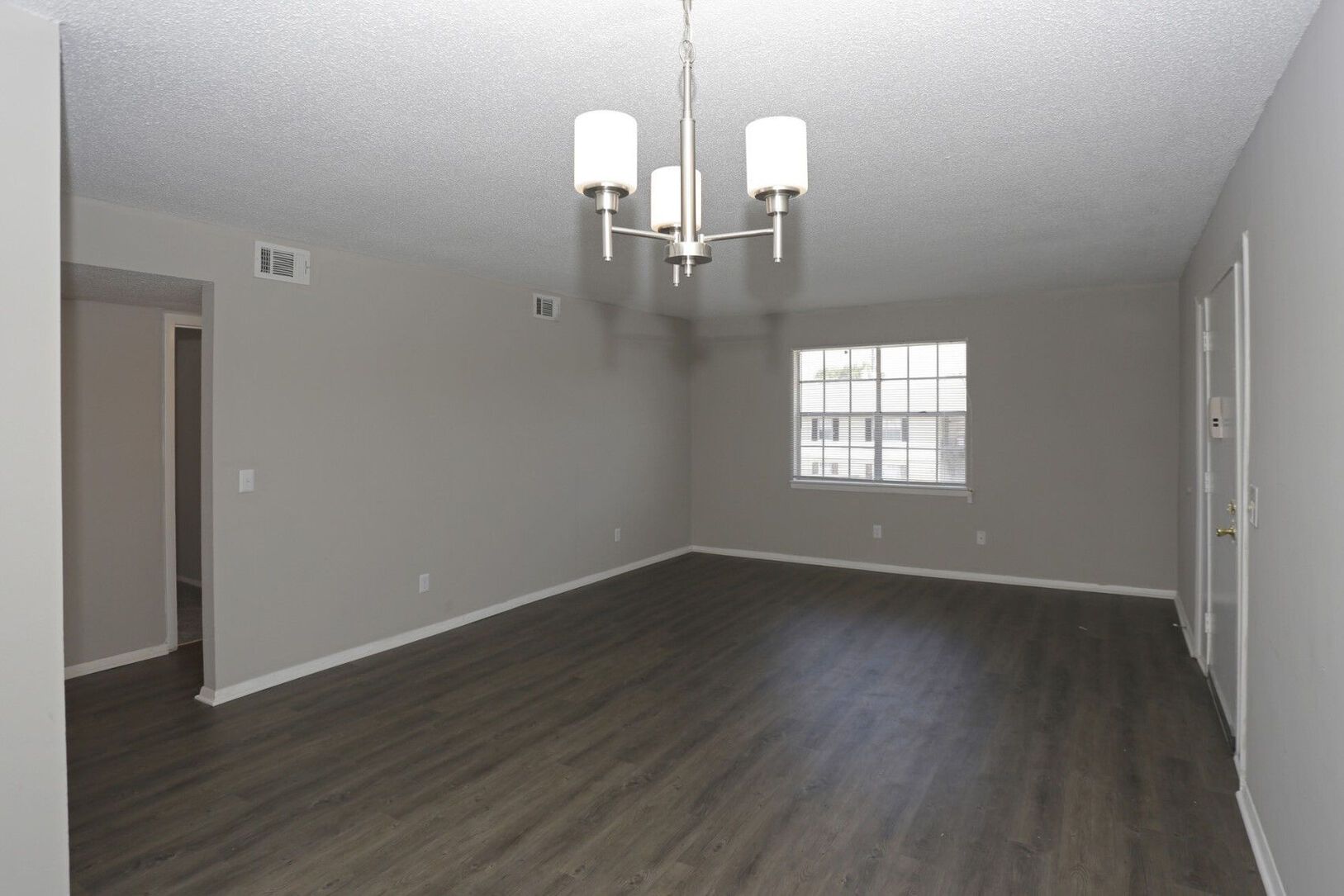 Empty living room with gray walls, dark wood-look flooring, a chandelier, and a window.