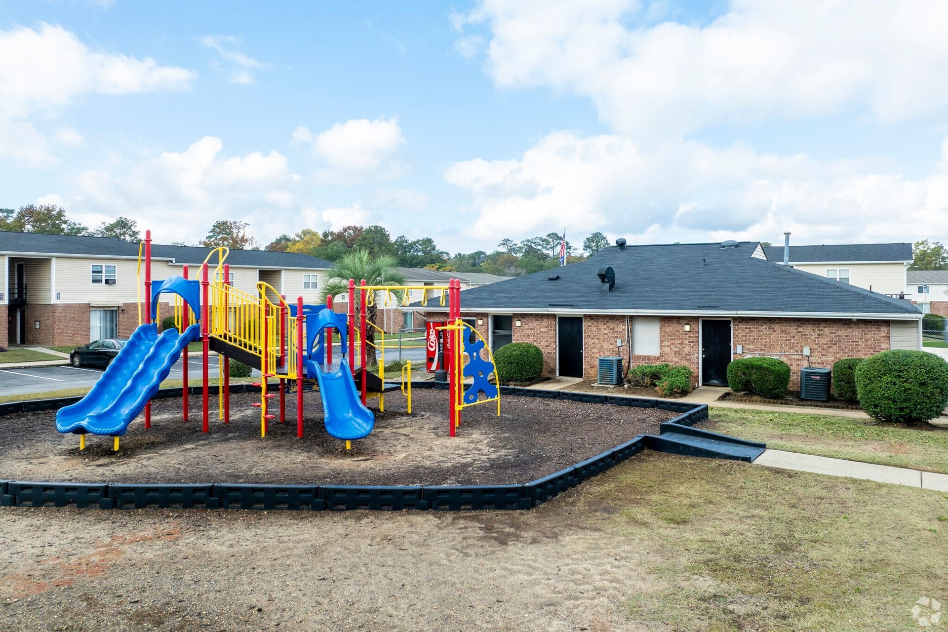 Playground with blue slides and colorful equipment in front of brick apartments under a cloudy sky.