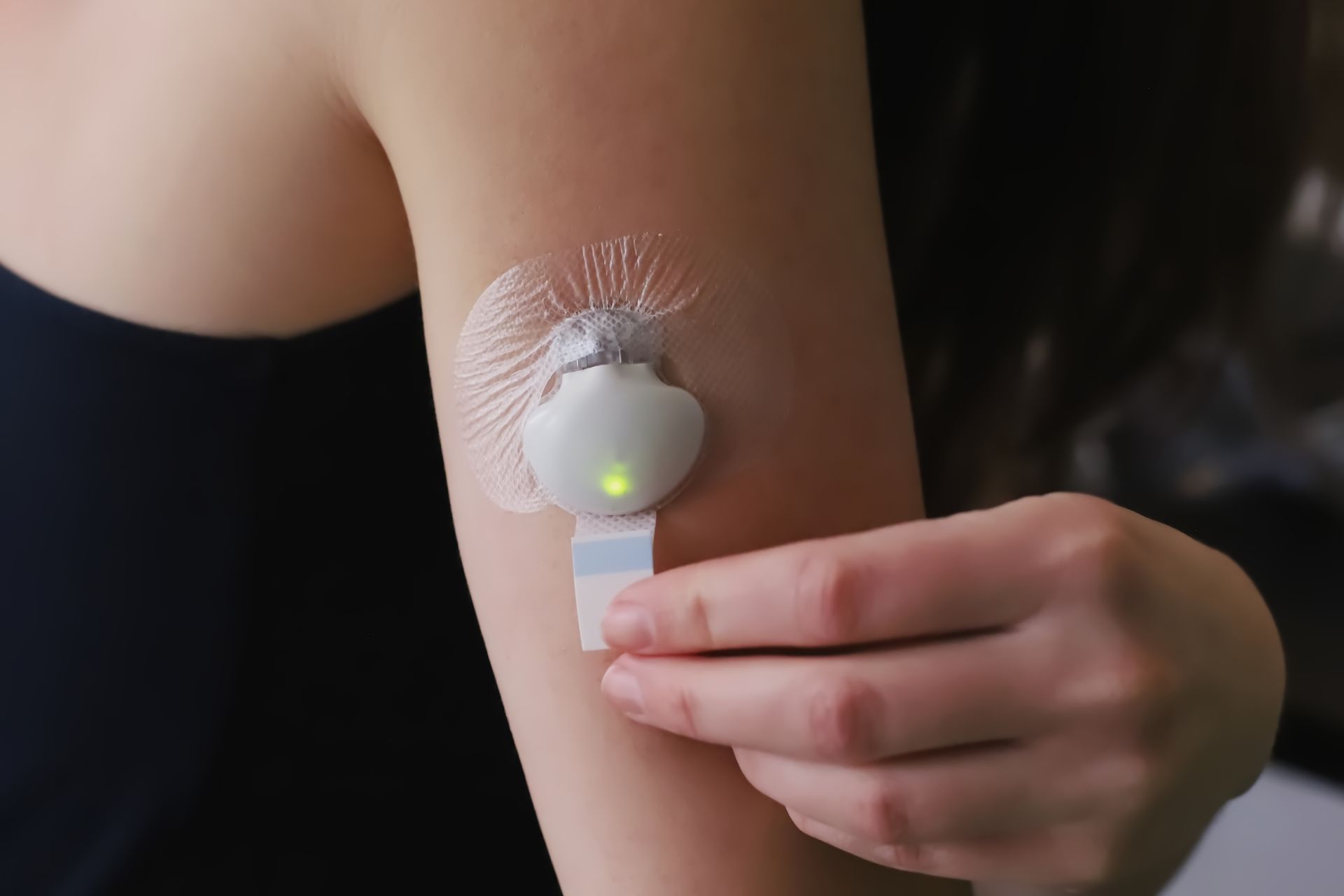 Person's arm with a white sensor on it. The sensor has a light on and is being held.