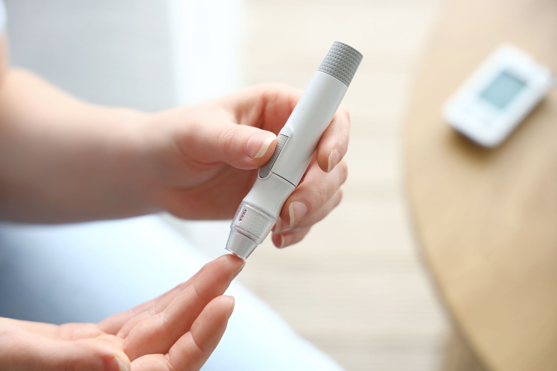 Person using a lancet to prick their finger, blood glucose meter in the background.