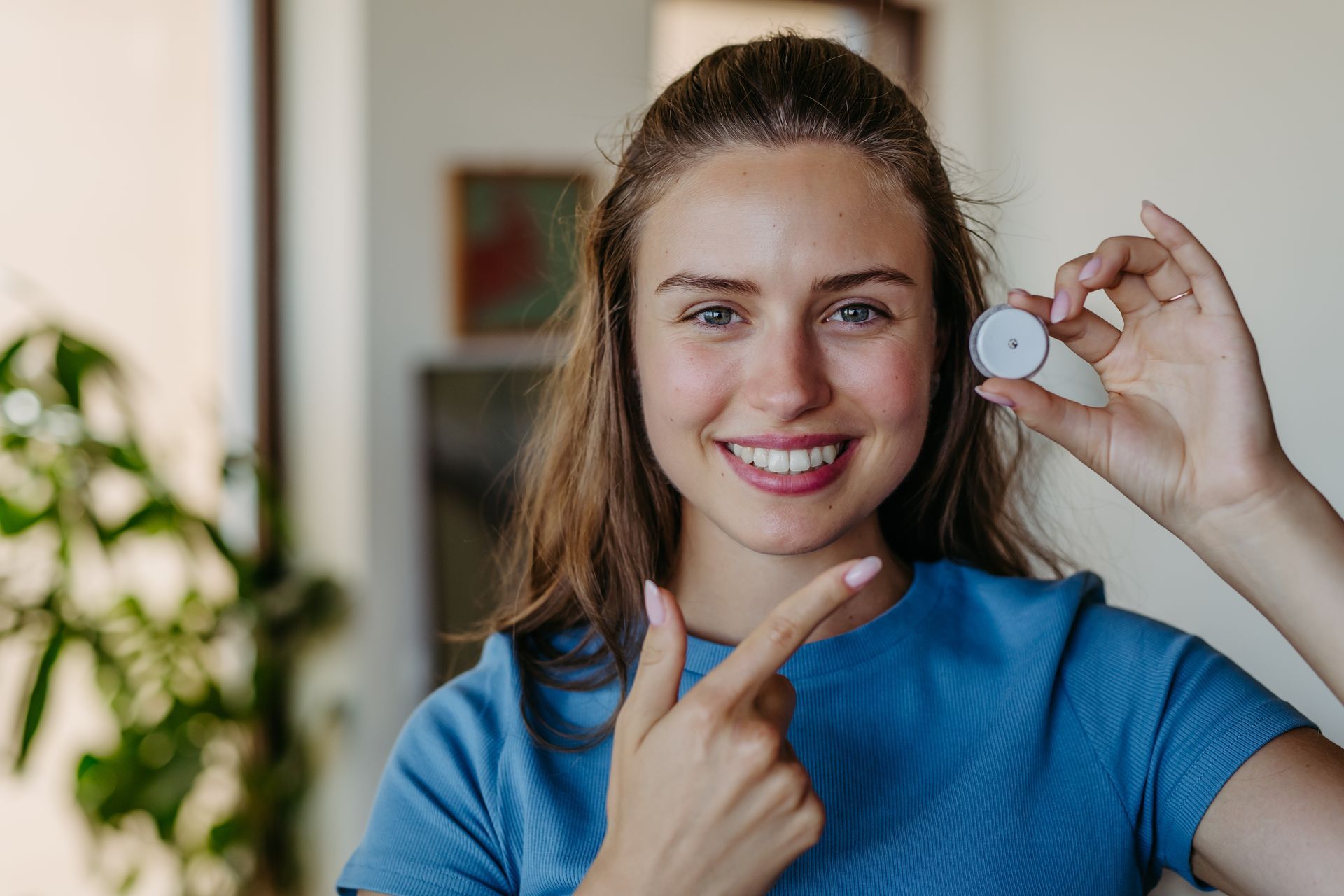 Woman smiling, holding and pointing to small white circular object. Inside.