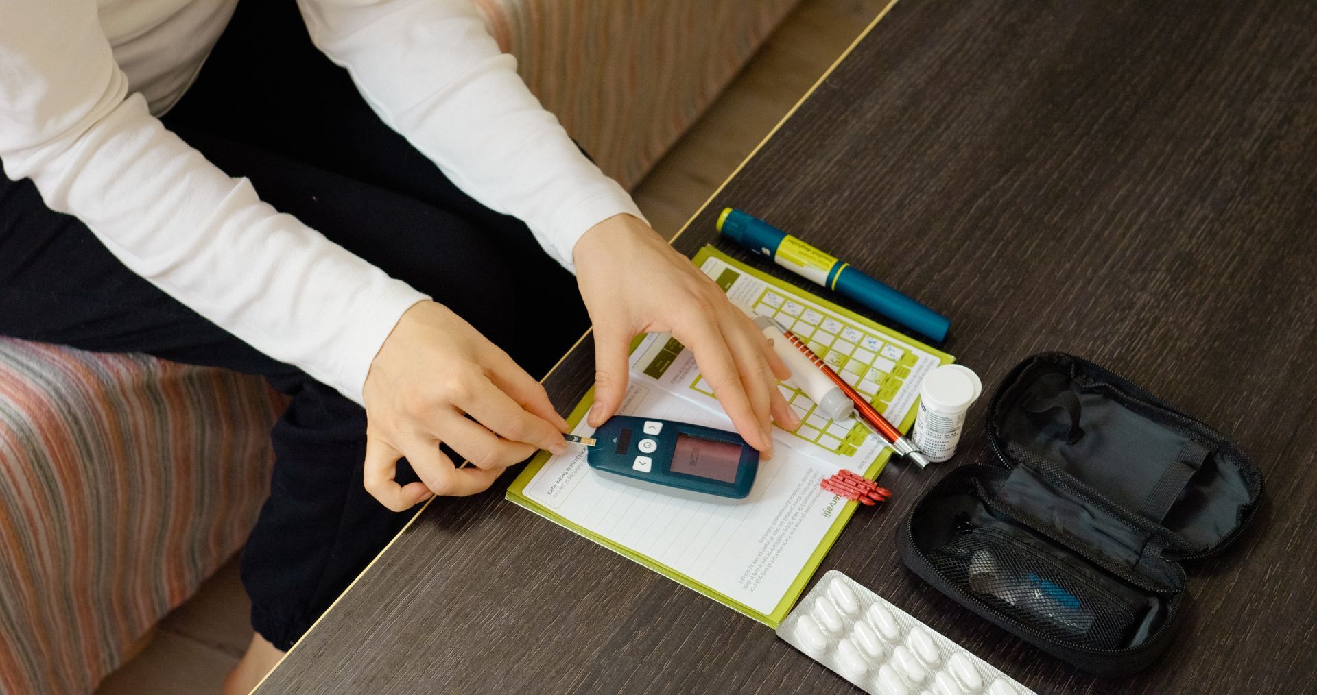 Person testing blood sugar with a glucose meter on a table with diabetes supplies.