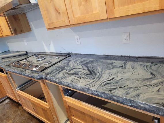 A kitchen with light wood cabinets, a black and white marble-patterned countertop, and an integrated gas stovetop.