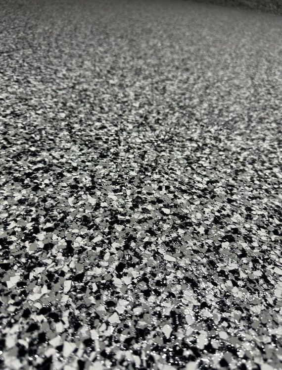 Close-up of a monochromatic garage floor coating with a speckled black, white, and gray vinyl chip texture.