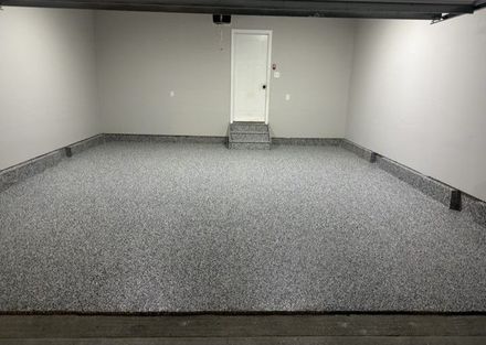 Empty garage with light gray walls, a white door, and a speckled gray epoxy floor coating with matching baseboards.