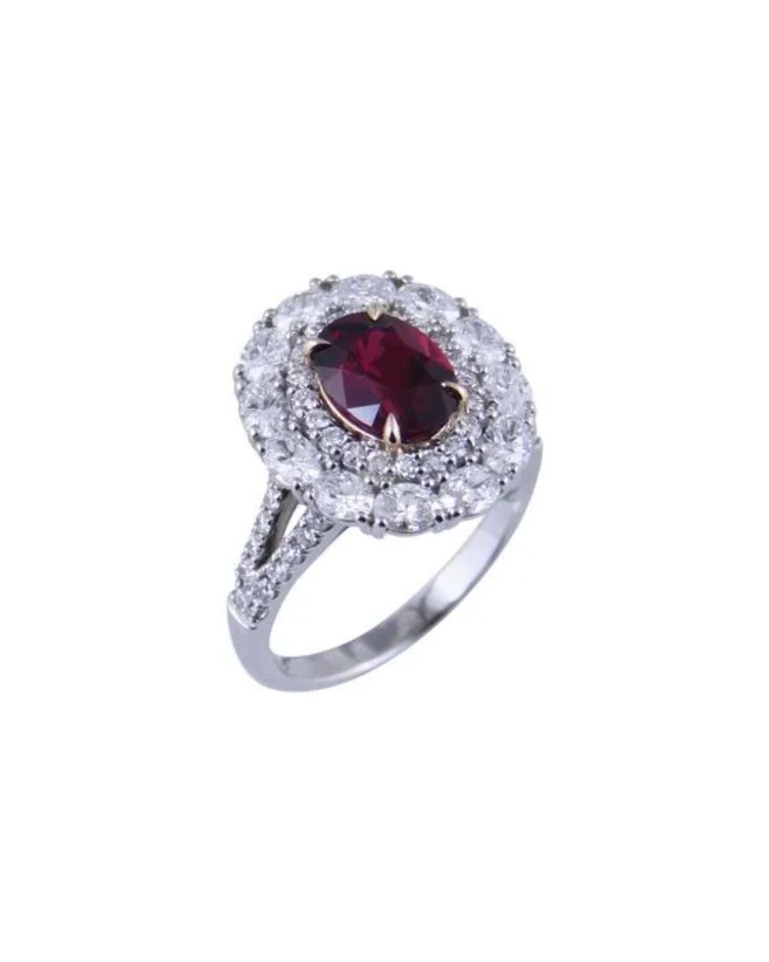 An oval red gemstone ring surrounded by a double halo of white diamonds on a split silver band against a white background.