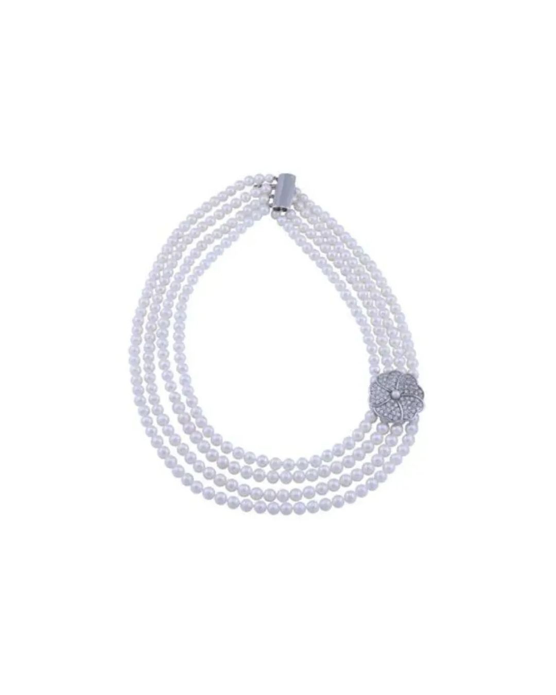 A four-strand white pearl necklace with a silver floral-shaped clasp encrusted with small clear crystals.