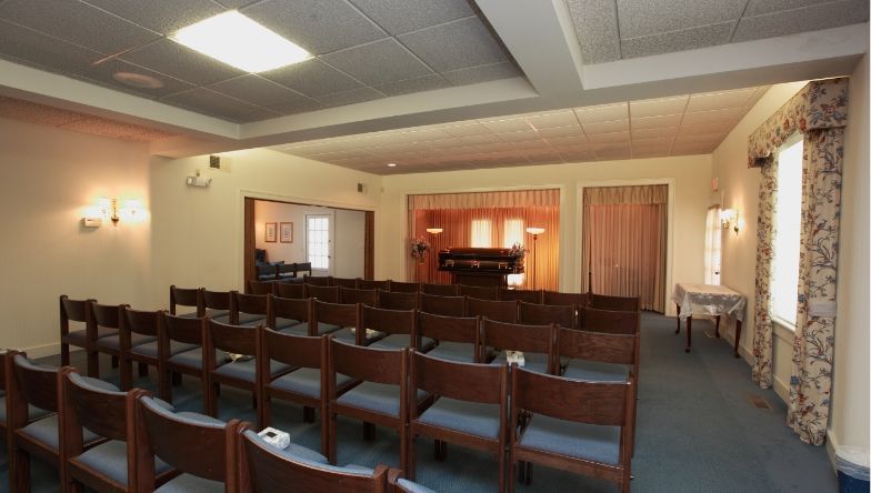 A room with rows of wooden chairs and a piano in the background.