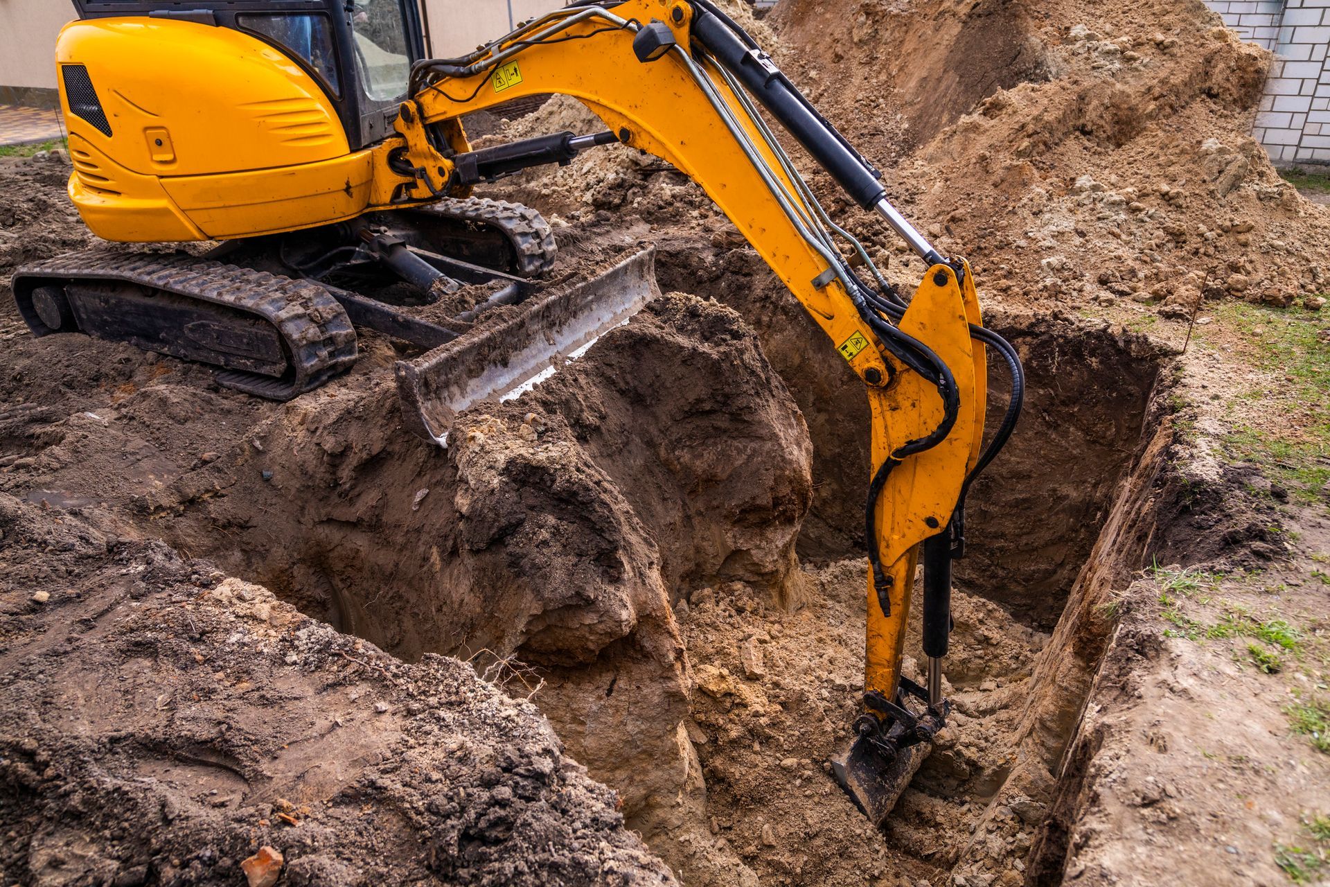 Yellow excavator digging in a dirt trench, with excavated soil piled nearby.