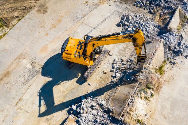 Yellow excavator demolishing concrete structure.