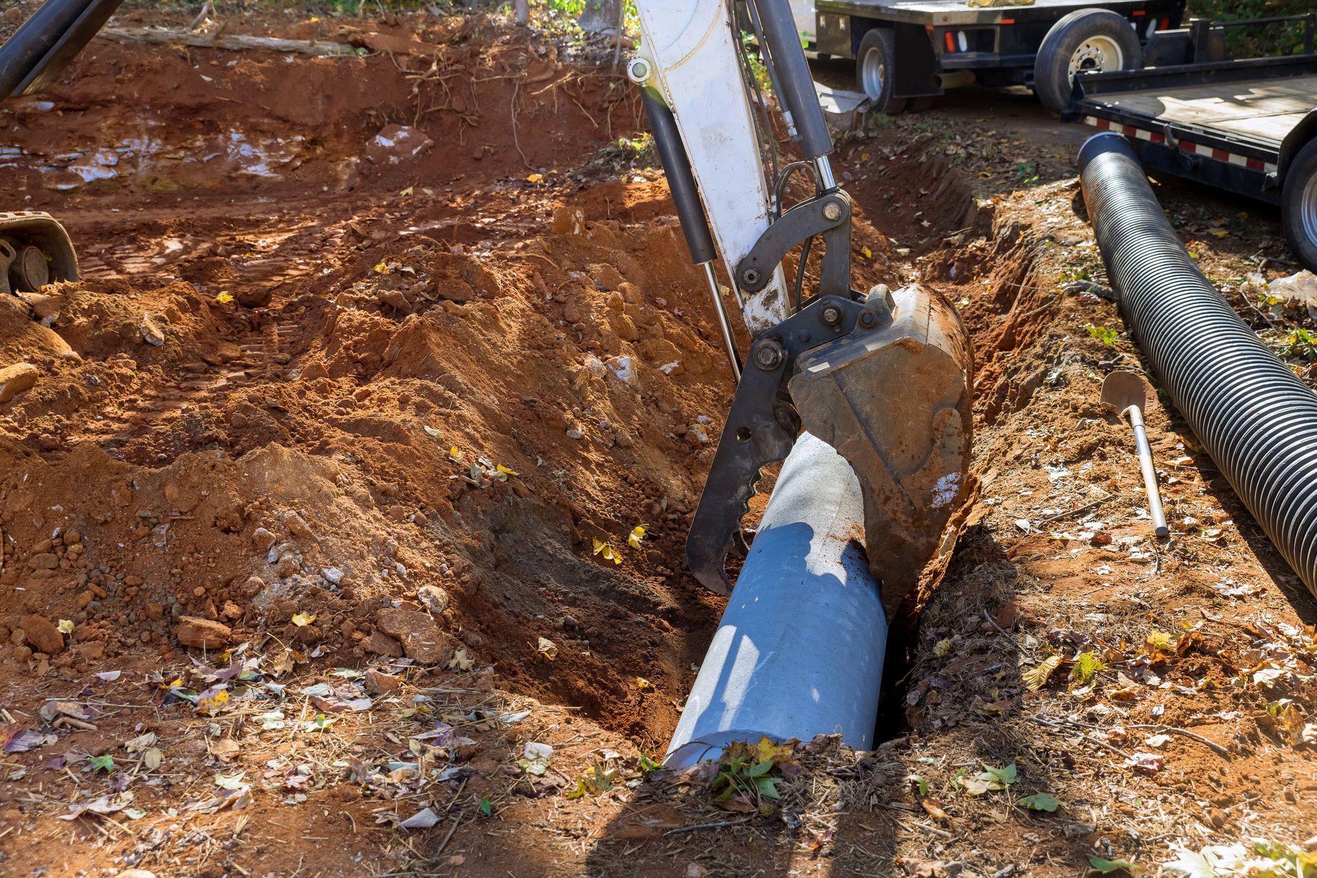 Excavator digging a trench around a blue pipe in dirt.