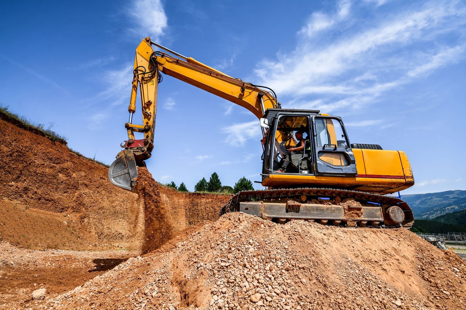 Yellow excavator digging into a mound of dirt on a sunny day.