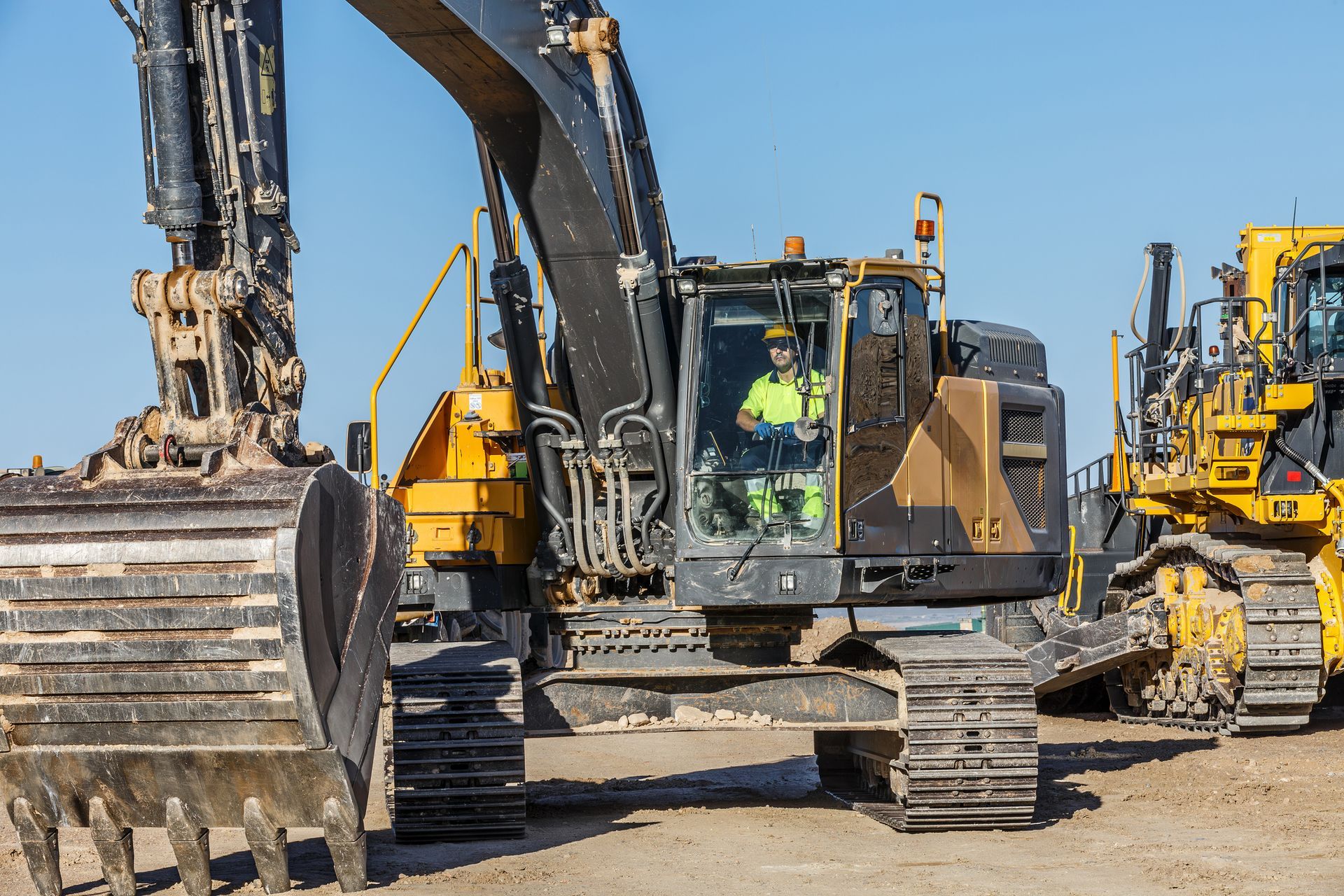 A construction worker operates a yellow excavator on a sunny day.