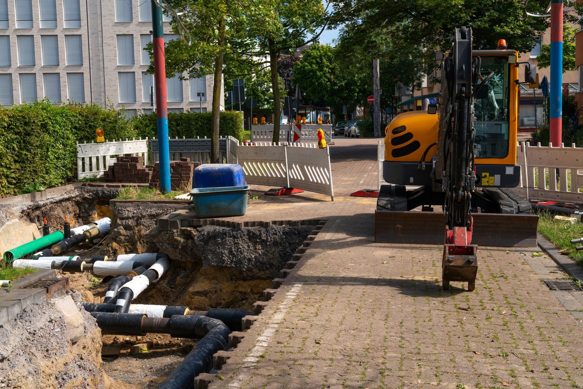 Construction site with exposed pipes, mini excavator, and fencing.