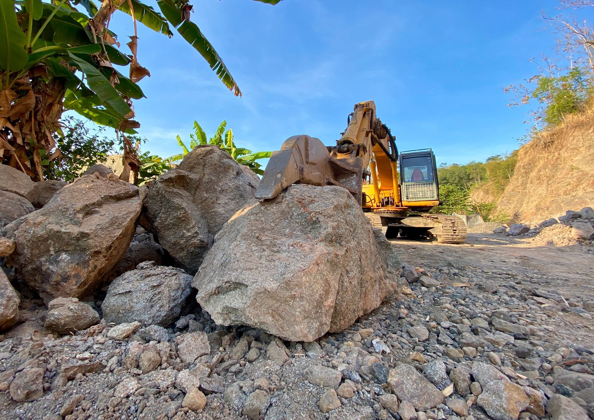Excavator next to large rocks and hillside on a sunny day.