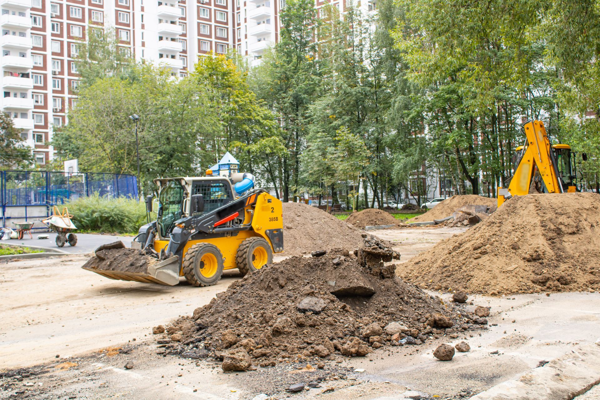 Yellow construction vehicles moving dirt on a construction site with a high-rise building in the background.