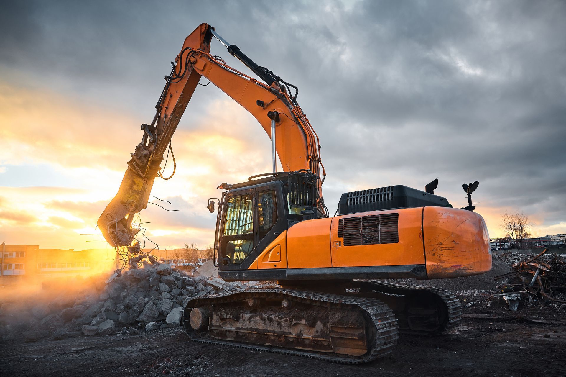 Orange excavator demolishing rubble against a sunset sky.