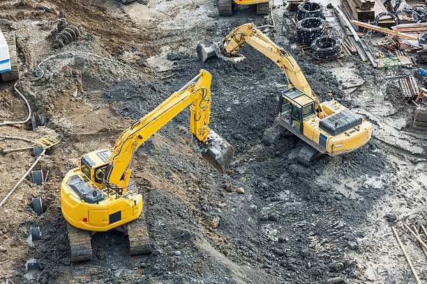 Two yellow excavators working on a construction site, digging into dirt.
