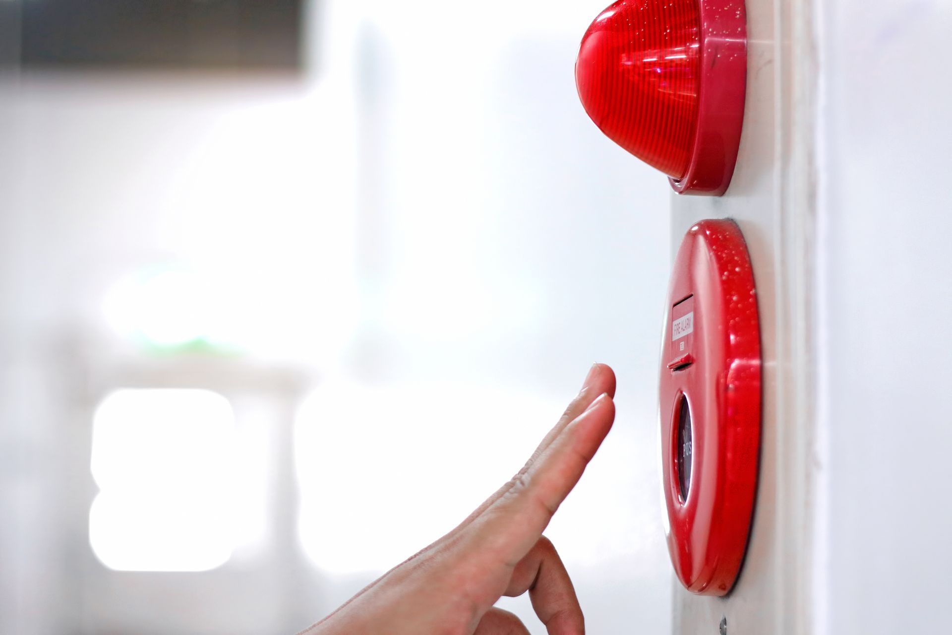 A person is pressing a red fire alarm button with their finger.