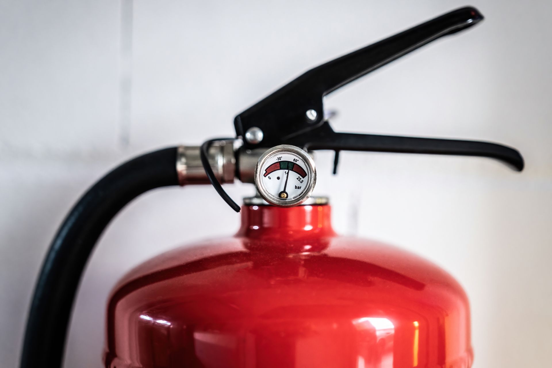 A close up of a red fire extinguisher against a white wall.