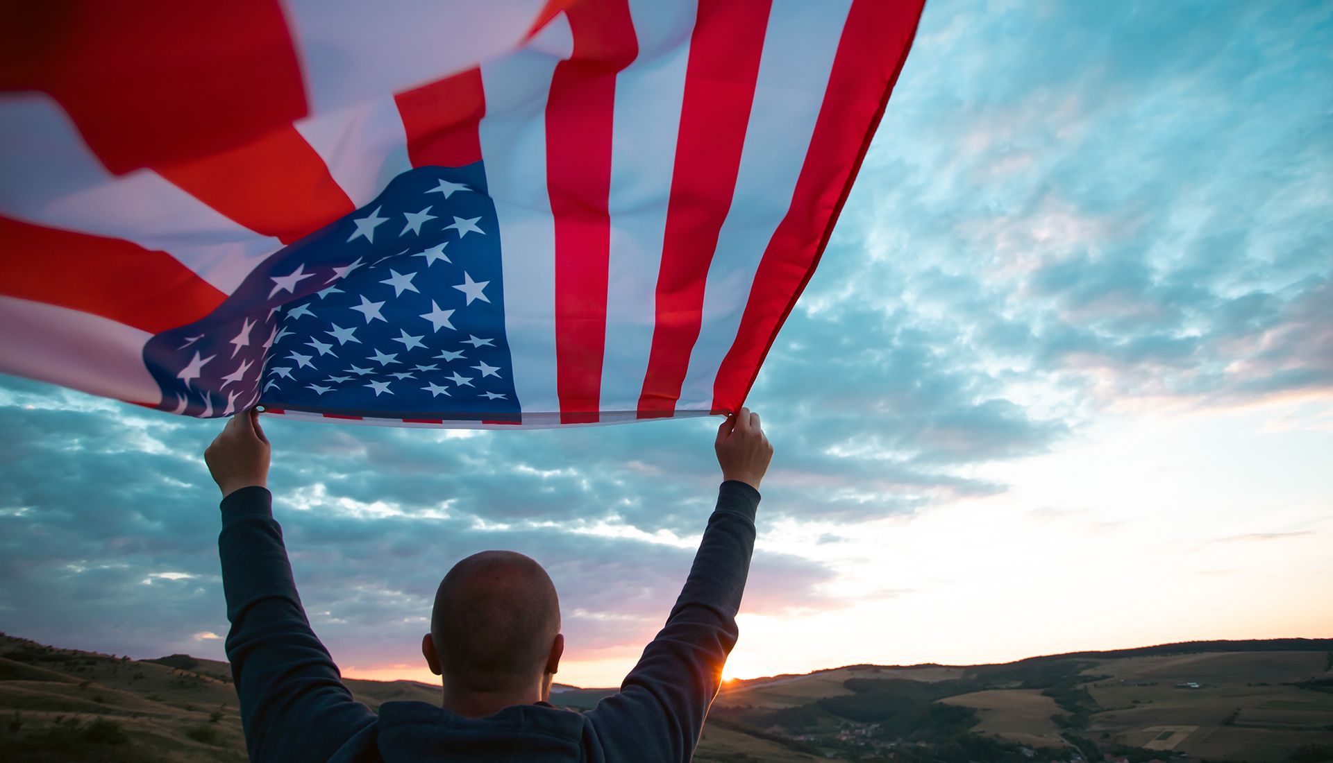 Person holding up an American flag against a sunset sky.