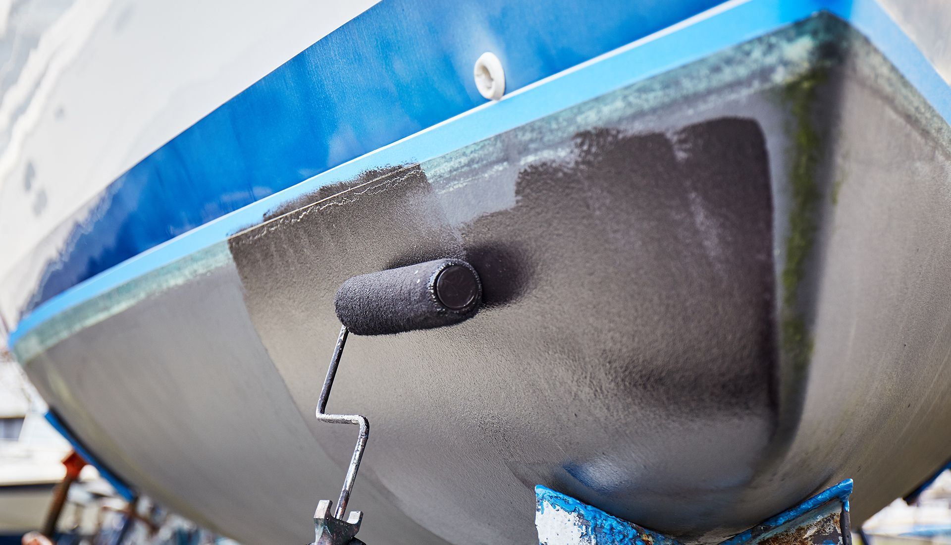 Boat hull being painted black with a roller. Blue and white boat.