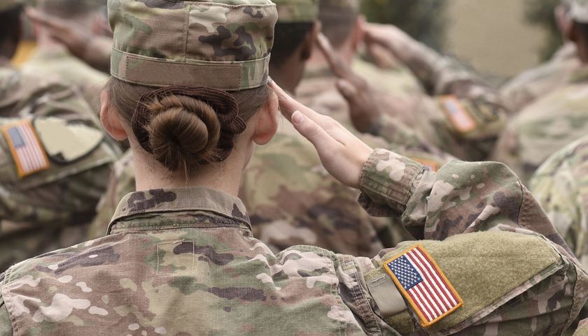 Soldiers in camouflage uniforms saluting outdoors, with American flag patch visible.