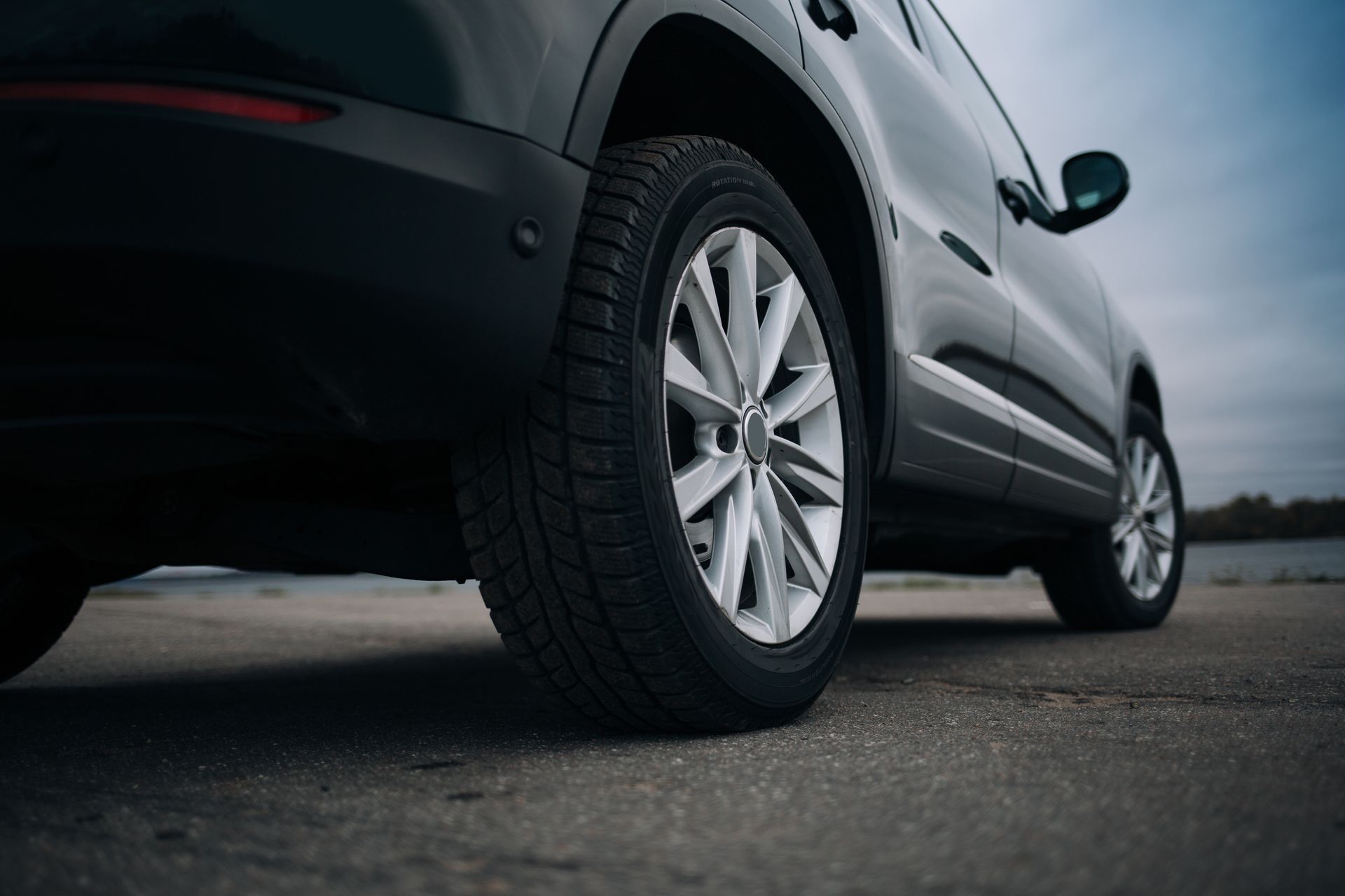 Dark SUV parked on a gray asphalt surface; cloudy sky in the background | Chet's Wheel Alignment