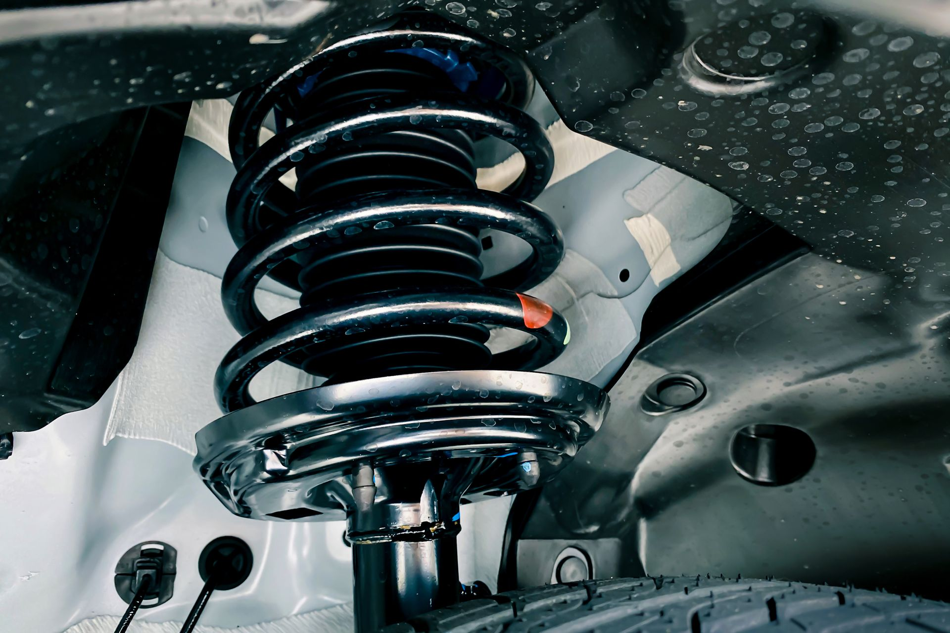 Car suspension system with black coil spring and shock absorber, viewed from below | Chet's Wheel Alignment