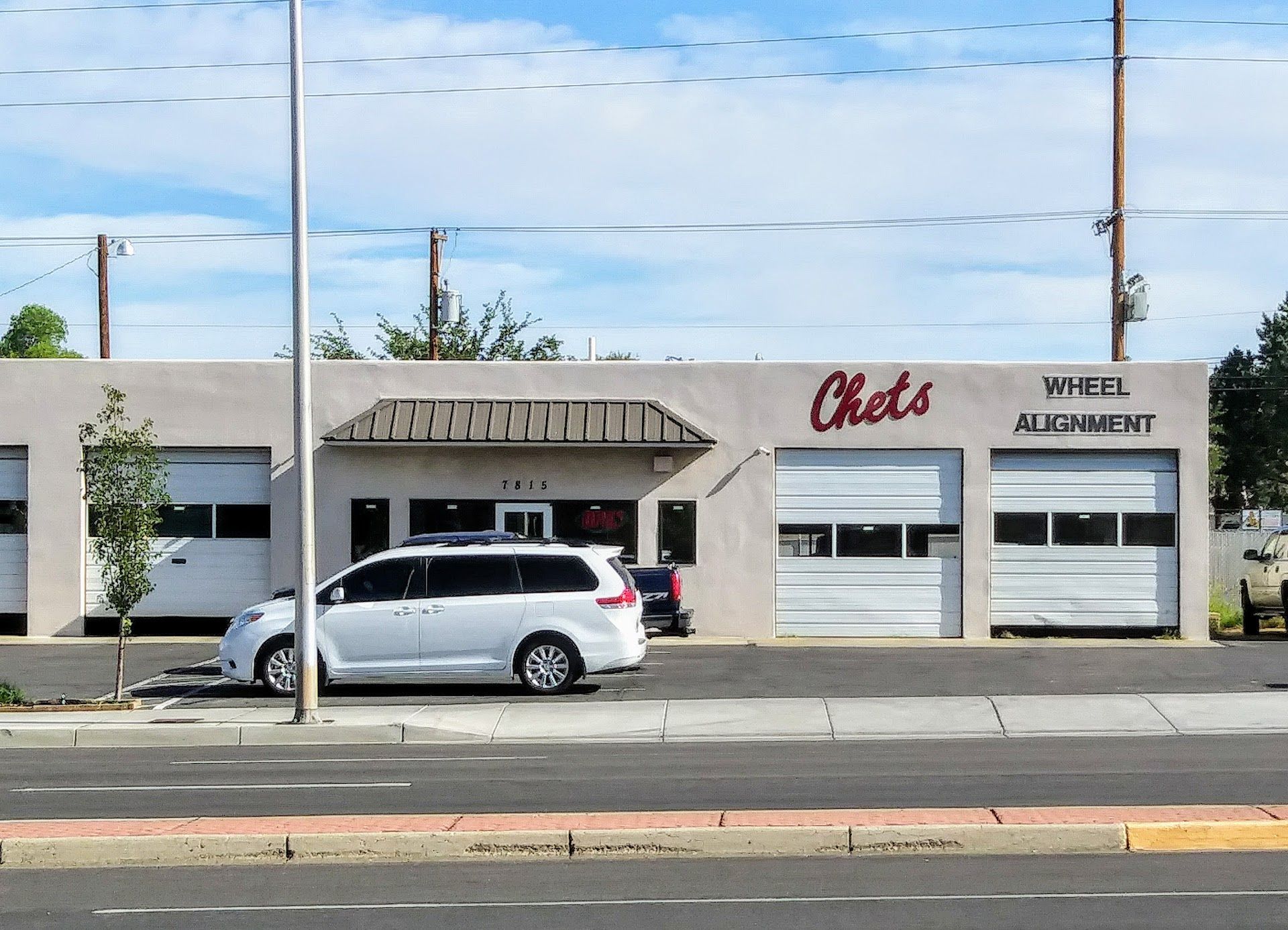 White minivan parked outside of Chet's Wheel Alignment auto shop with closed garage doors under a blue sky | Chet's Wheel Alignment