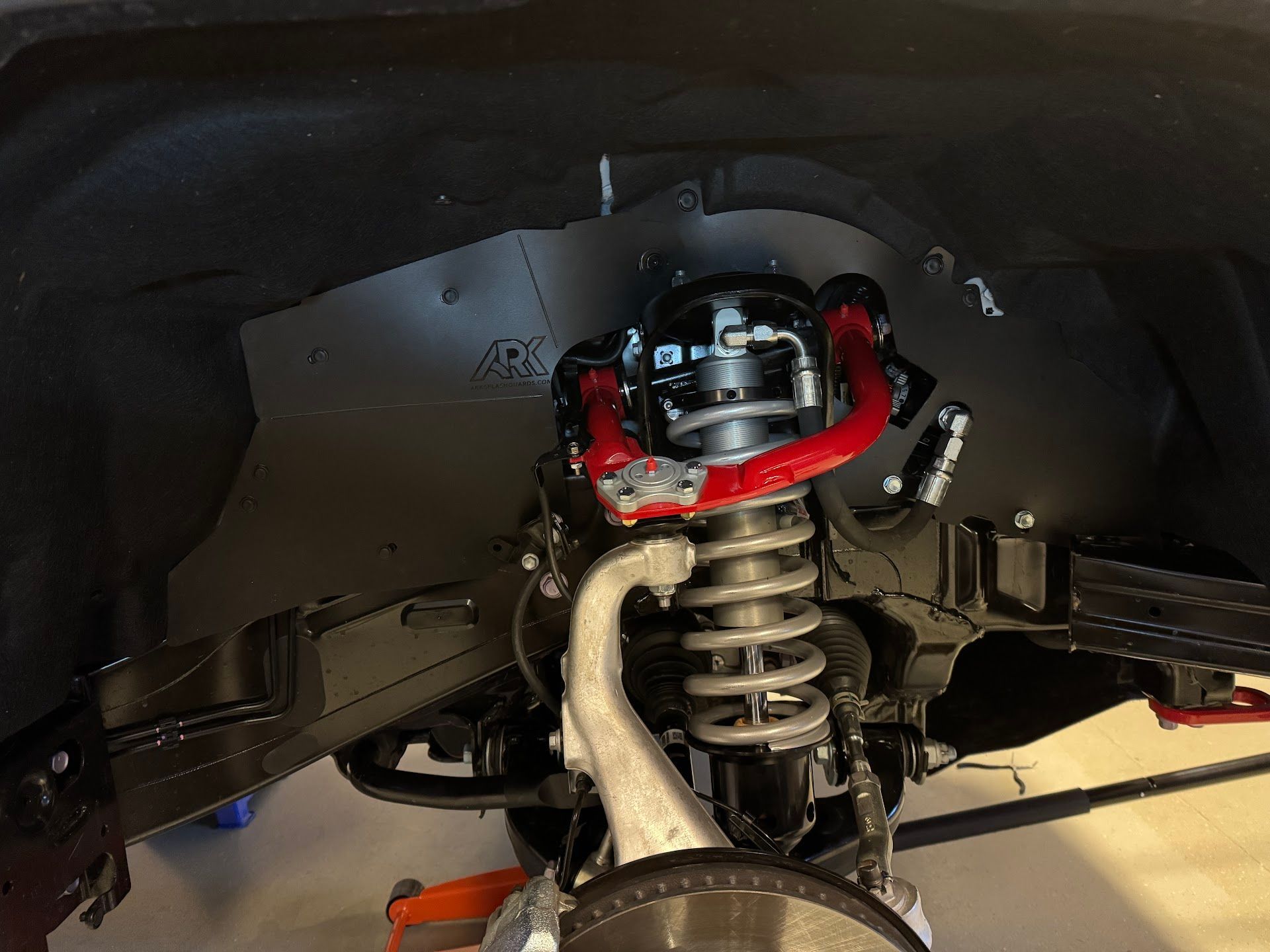 Truck suspension with red upper control arm, coil spring, and black wheel well | Chet's Wheel Alignment