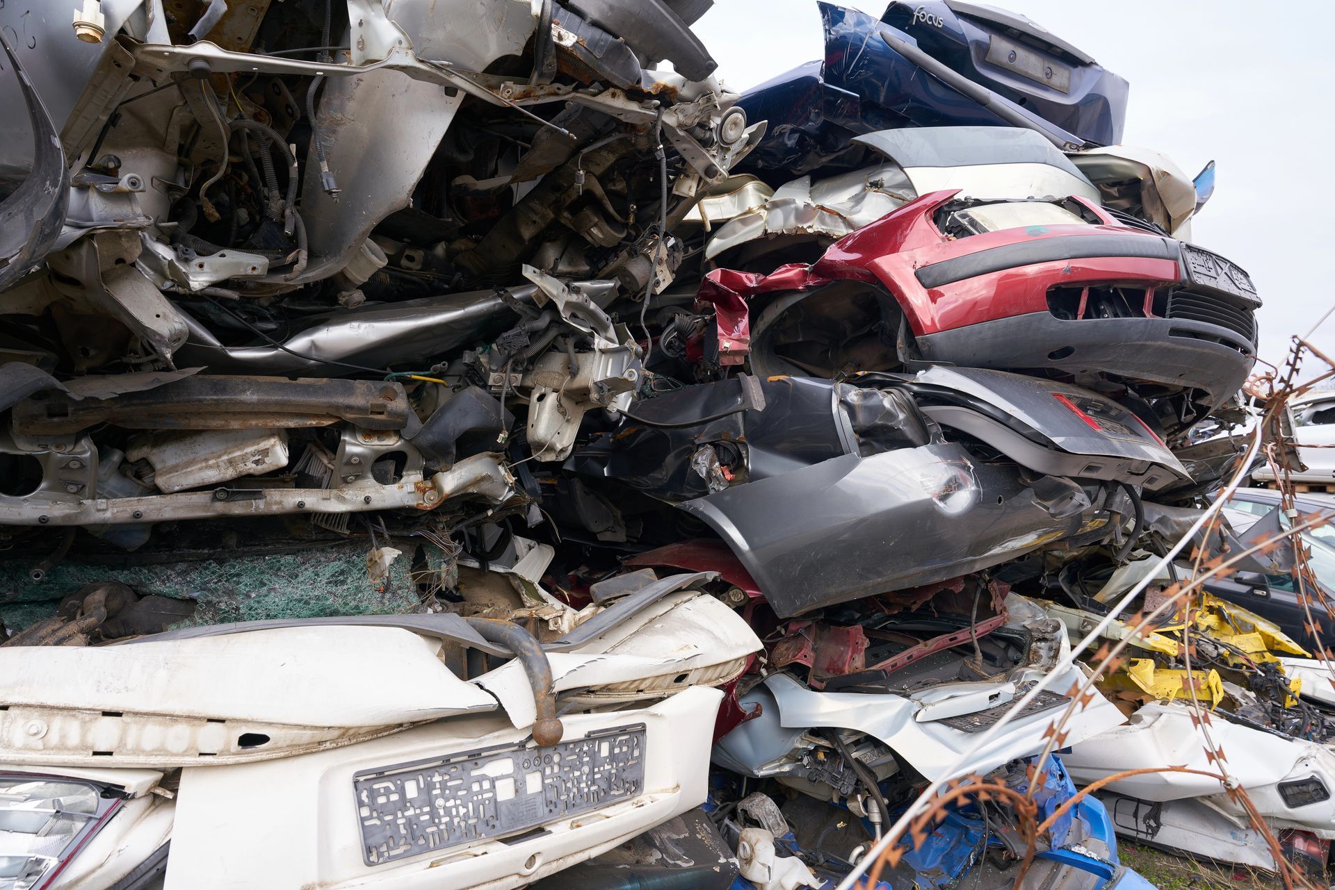 Pile of crushed car parts at a junkyard; various colors visible, including red, blue, and white.