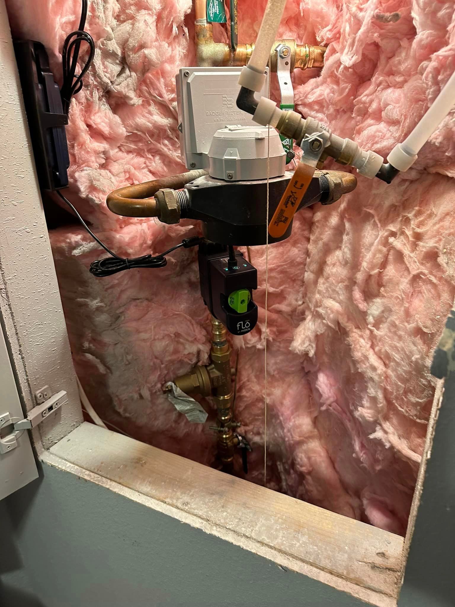 A close up of a water meter in a room with pink insulation.