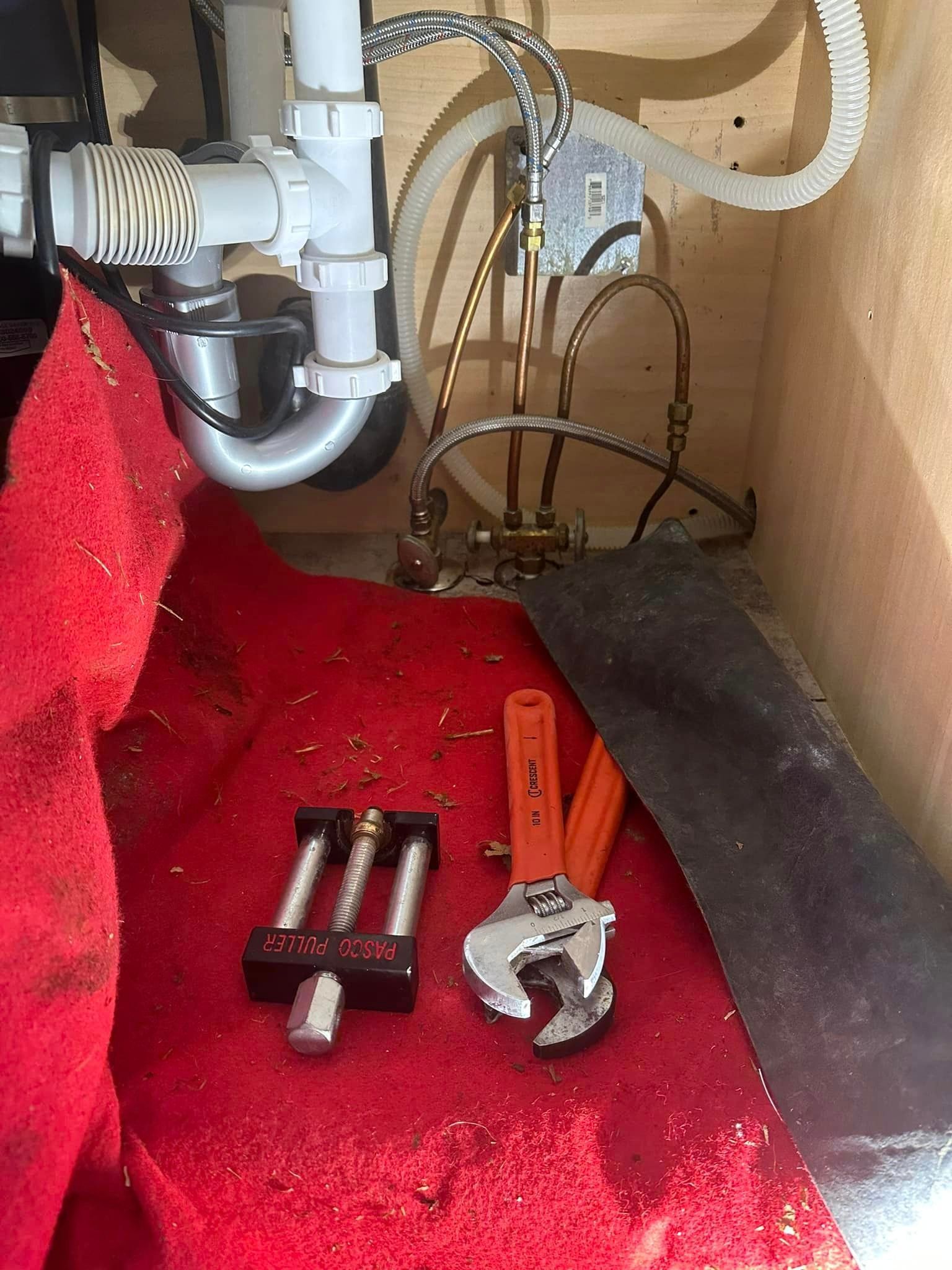A wrench and pliers are sitting on a red towel under a sink.
