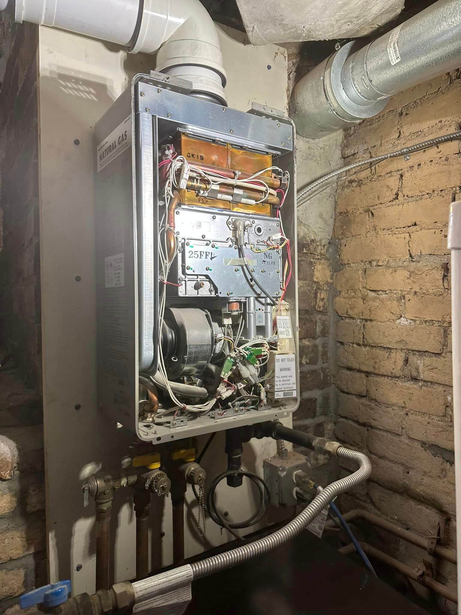 A water heater is sitting in a basement next to a brick wall.