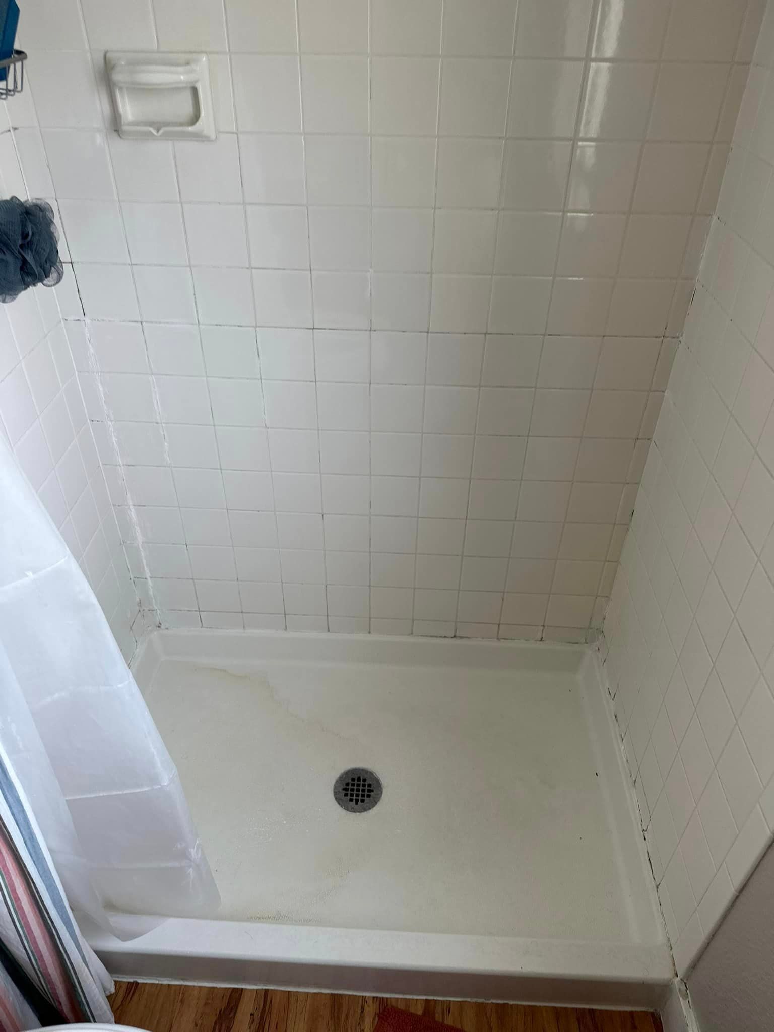A shower stall with white tiles and a drain in a bathroom.